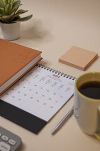 A desk setup with a weekly planner, colorful pens, and a coffee cup.