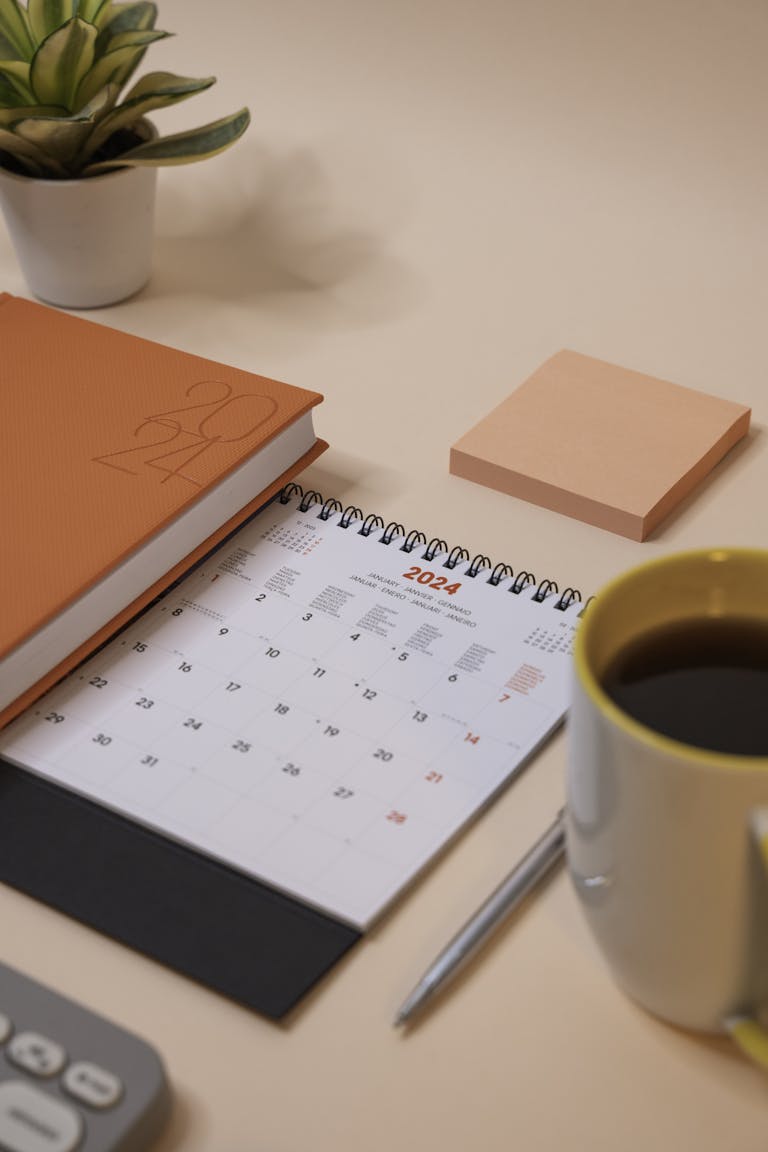 A desk setup with a weekly planner, colorful pens, and a coffee cup.