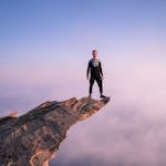 A person confidently standing at the edge of a cliff overlooking a sunrise, symbolizing courage and new beginnings.