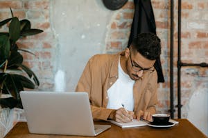A person yawning at their desk with coffee in hand and a cluttered background.
