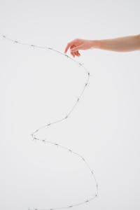 A hand gently touches barbed wire on a white background, symbolizing tension.