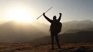 A person standing on a mountain peak with arms raised in triumph, symbolizing growth and achievement.