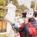 A masked protestor in West Java, Indonesia, using a megaphone during a daytime demonstration.