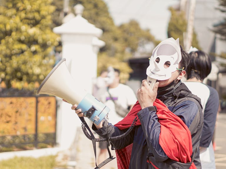 A masked protestor in West Java, Indonesia, using a megaphone during a daytime demonstration.