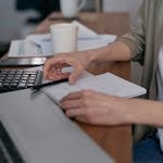 A person sitting at a desk with financial documents, a calculator, and a laptop, focused on budgeting.