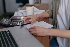 A person sitting at a desk with financial documents, a calculator, and a laptop, focused on budgeting.