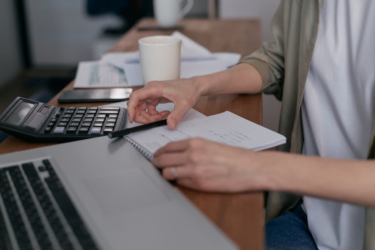 A person sitting at a desk with financial documents, a calculator, and a laptop, focused on budgeting.
