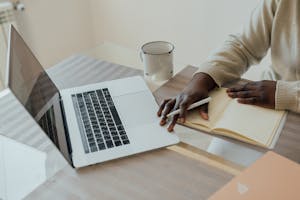 A person typing journal entries on a laptop in a cozy, minimalist workspace.