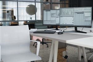 A clean, modern home office with natural light, ergonomic chair, and dual monitors.