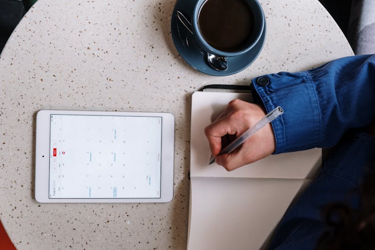 A neatly organized digital calendar on a screen beside a cup of coffee and a notebook.