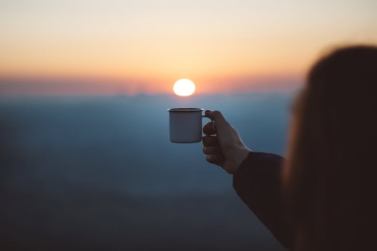 Peaceful sunrise with coffee, notebook, and a person stretching toward the sun
