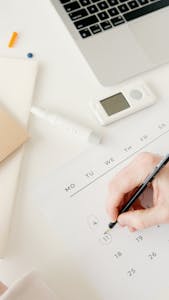 A person using a planner or digital calendar with a clock in the background