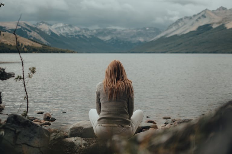 A peaceful person sitting alone by a lake with a phone turned off beside them.