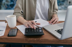A person using a planner or digital calendar with a cup of coffee beside them