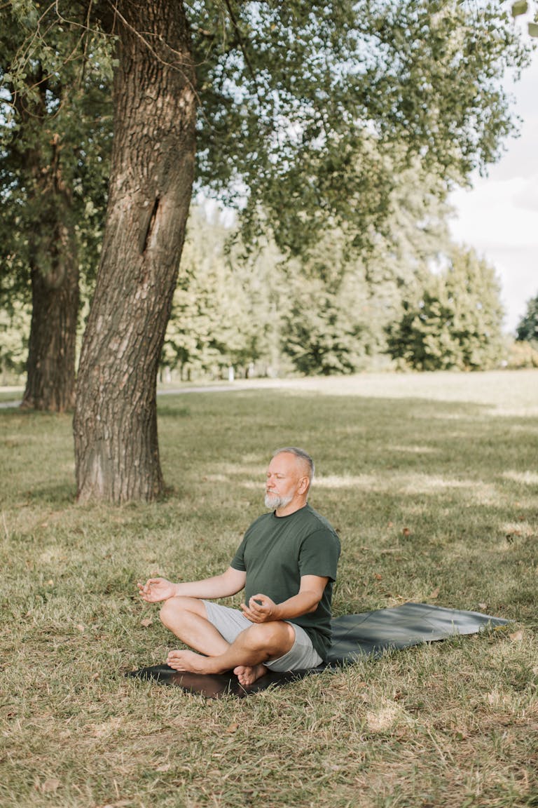A person practicing mindfulness in a serene park or nature setting, sitting cross-legged with eyes closed