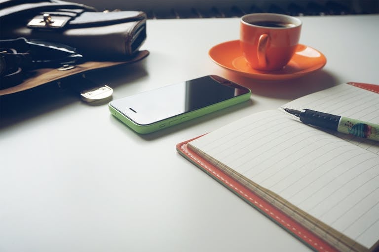 An open journal on a clean desk with a pen and a cup of tea beside it.