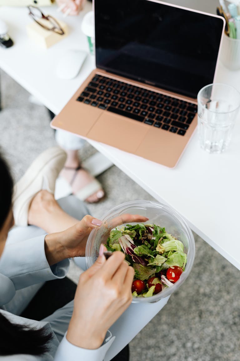 A person eating a healthy meal while working on a laptop