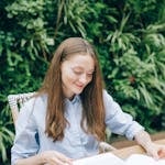 A person calmly reading a book in natural light, with a phone face-down on the table nearby.