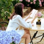 A person reading a book in nature with their phone face-down on a table nearby.