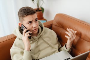 A person looking at their watch in frustration while multitasking with phone and laptop.