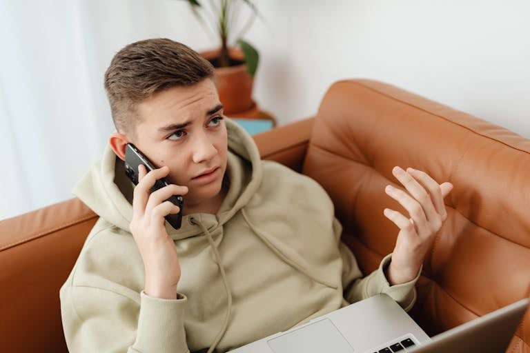 A person looking at their watch in frustration while multitasking with phone and laptop.