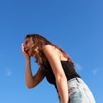 A young woman in casual attire laughing outdoors against a vibrant blue sky, radiating happiness.