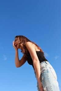 A young woman in casual attire laughing outdoors against a vibrant blue sky, radiating happiness.