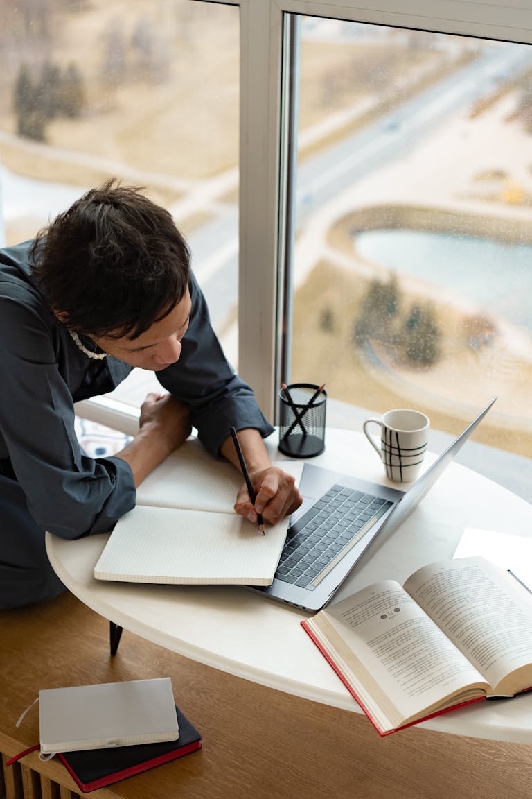 A person reading a book at a desk, surrounded by notes, coffee, and a laptop showing online courses.
