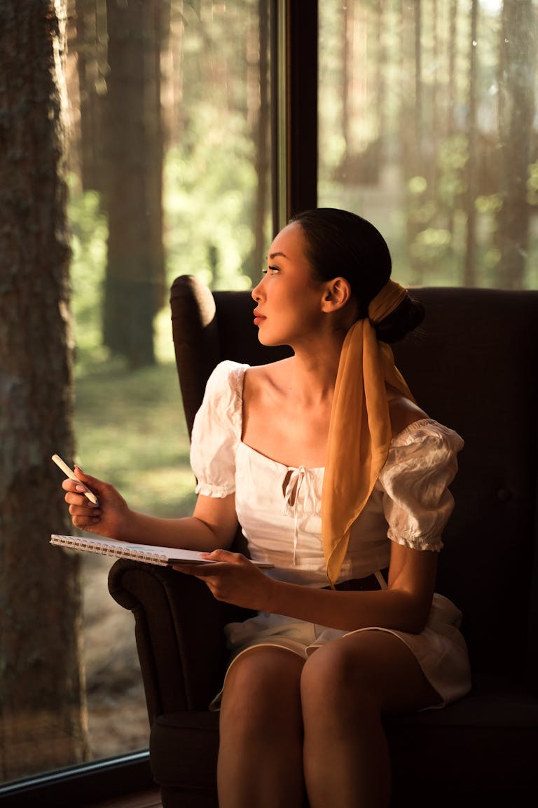 A person staring peacefully out a window with a journal nearby, no devices in sight.