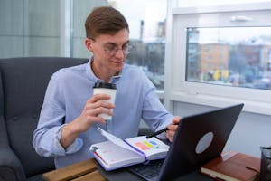 A person with a focused expression, working at a desk with a well-organized planner, a laptop, and a cup of coffee.