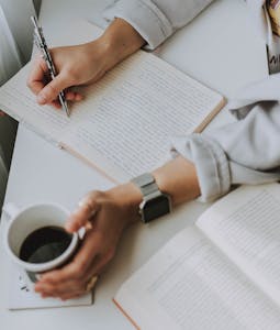A person journaling or reviewing a planner on a quiet Sunday morning with a cup of coffee.