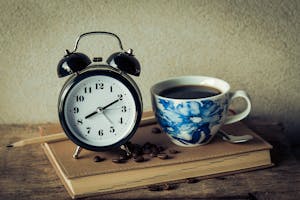 A desk with a planner, clock, and coffee cup