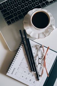 A desktop setup with a calendar, notebook, and coffee cup—mid-planning session.