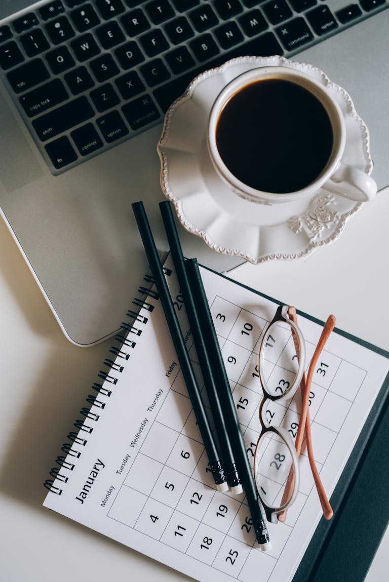A desktop setup with a calendar, notebook, and coffee cup—mid-planning session.