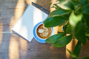 A checklist beside a cup of coffee and journal in the morning sunlight