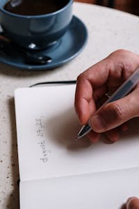 A person writing in a planner, with a coffee cup beside them, symbolizing focus and productivity.