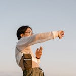 Joyful young woman stretching arms in a sunny field, embracing freedom and nature.