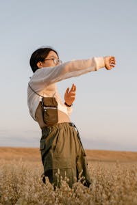 Joyful young woman stretching arms in a sunny field, embracing freedom and nature.