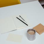 A clean, white workspace with a single notebook, pen, and coffee mug.