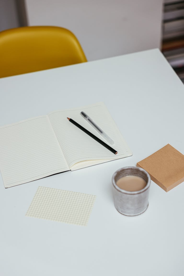 A clean, white workspace with a single notebook, pen, and coffee mug.