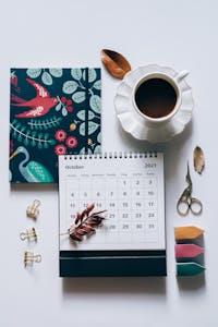 A colorful calendar planner with neatly arranged time blocks and a cup of coffee beside it.