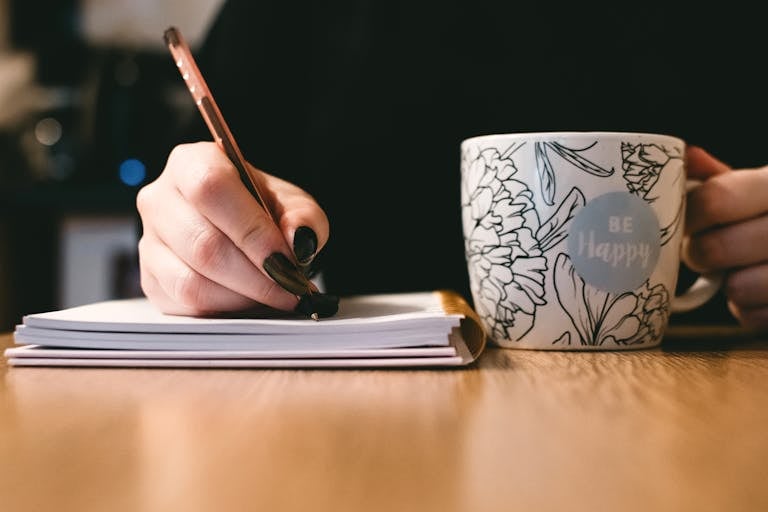 A person writing goals on a notebook with a coffee mug beside them