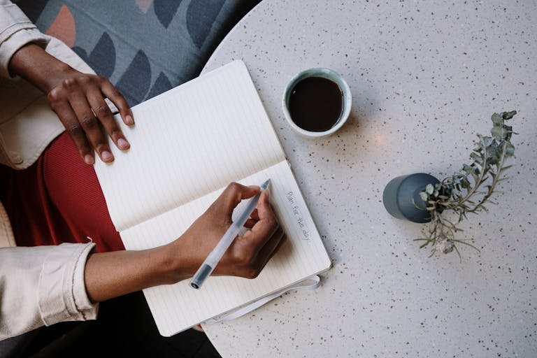 A person journaling with a planner, calendar, and coffee beside them.