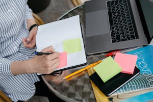 A person checking off a tiny task on a sticky note beside a laptop