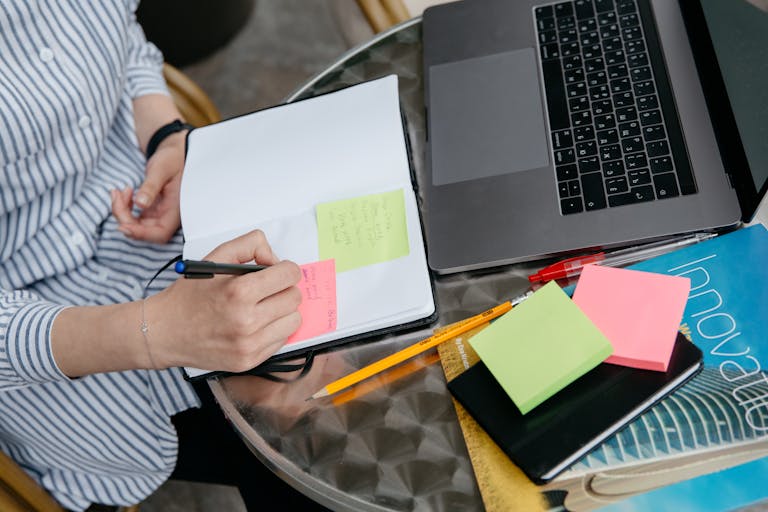 A person checking off a tiny task on a sticky note beside a laptop