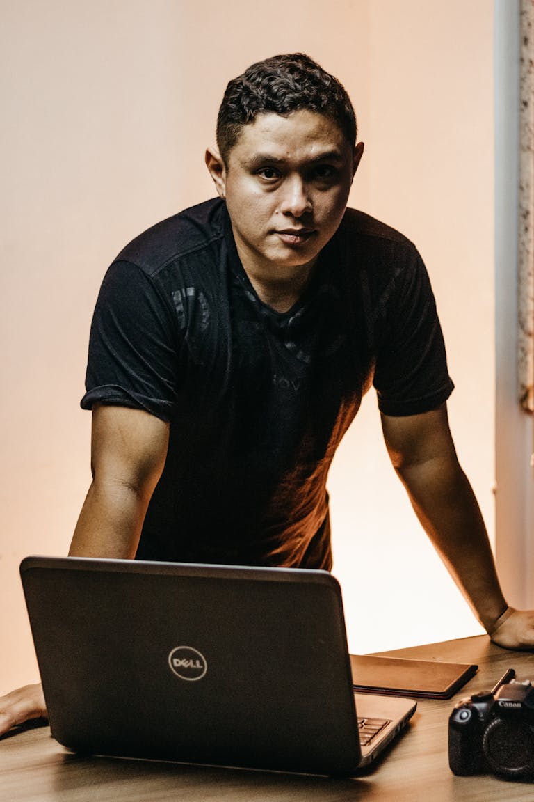 Portrait of a confident man leaning on a desk with a laptop, embodying modern work life.