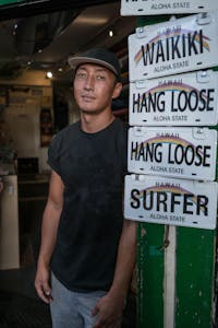Portrait of a man standing by a display of Hawaii-themed license plates in a shop.