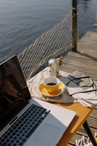 A person meditating in the morning sunlight with a journal, coffee, and laptop neatly organized on a desk.