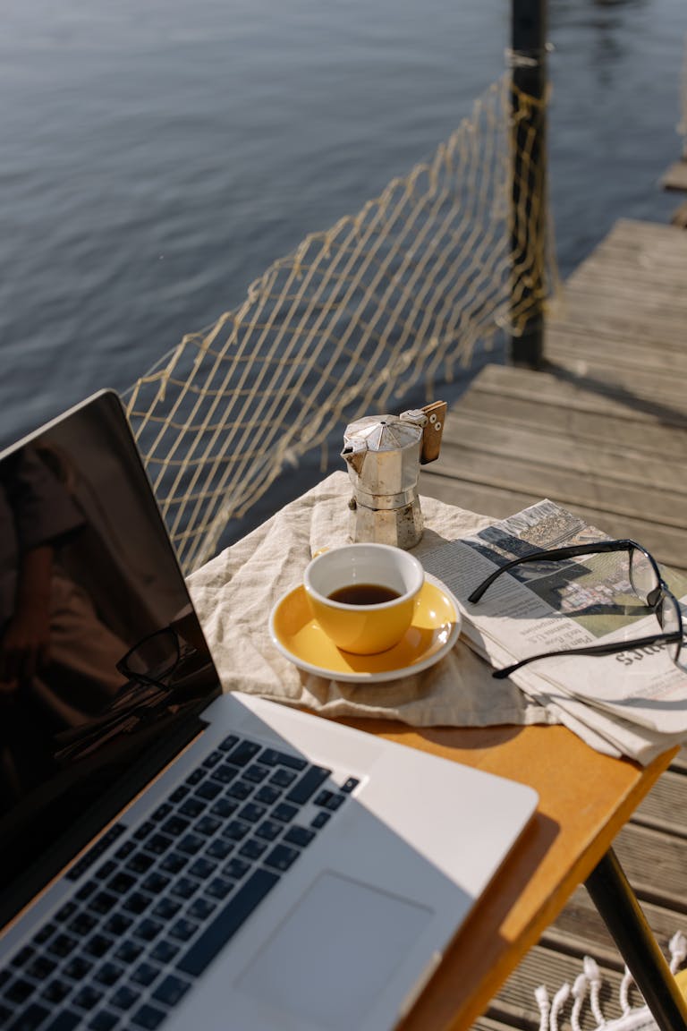 A person meditating in the morning sunlight with a journal, coffee, and laptop neatly organized on a desk.