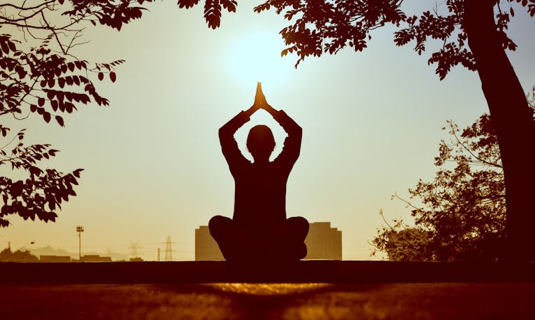 A person meditating outdoors with their phone turned off beside them